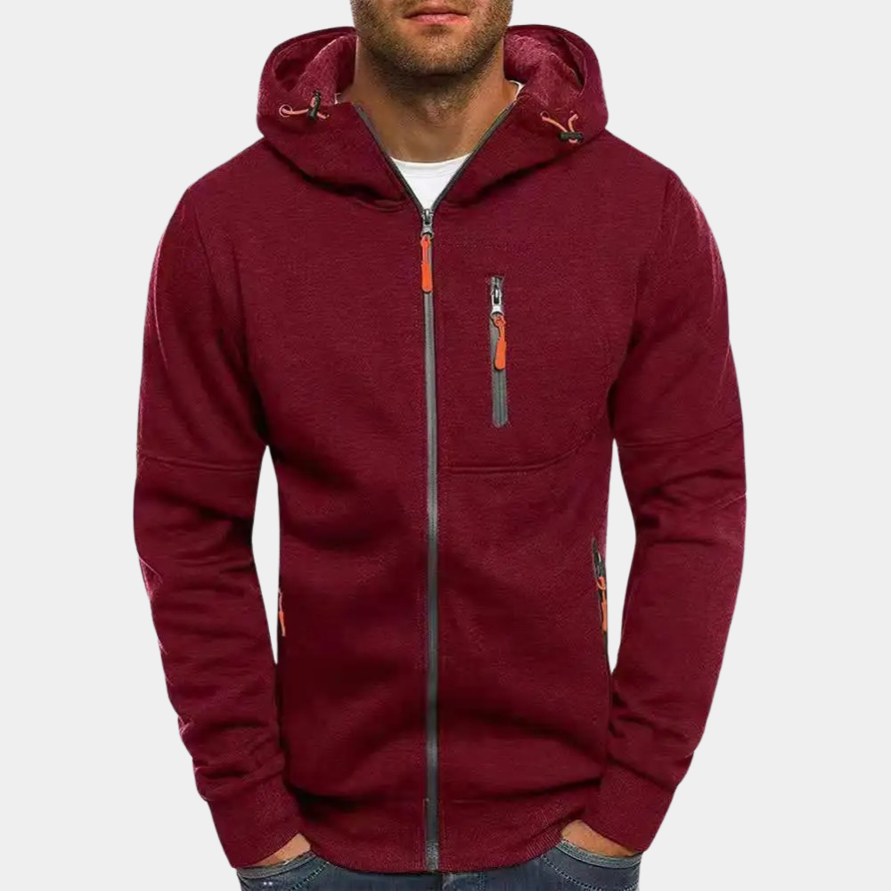 Homme portant un sweat à capuche bordeaux avec fermeture éclair, poches zippées et cordons. Mode décontractée, vêtement automne-hiver tendance.