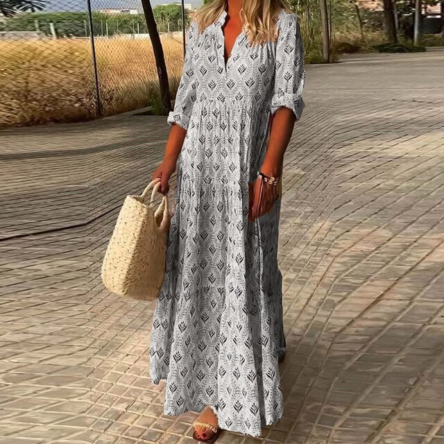 Femme en robe longue bohème imprimée, tenant un sac en osier, marchant sur un chemin pavé. Mode estivale, style décontracté chic.