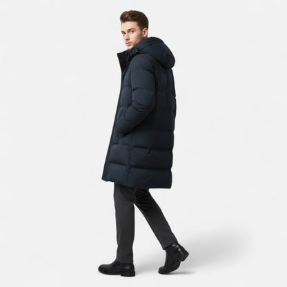 Homme portant un manteau d'hiver long et noir, style doudoune, avec capuche, marchant sur fond blanc. Mode masculine, vêtements chauds, hiver.