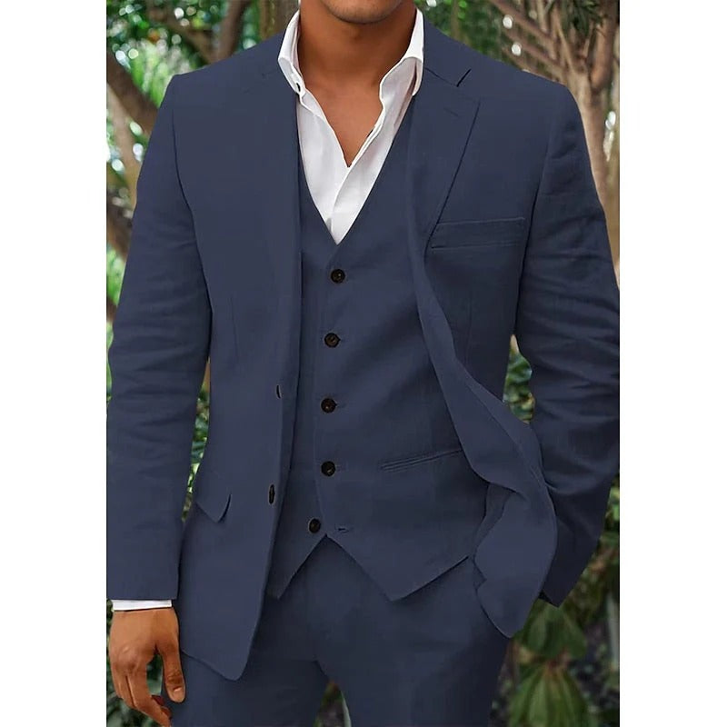 Homme en costume bleu marine élégant avec gilet, chemise blanche, posant devant un fond de verdure. Mode masculine, tenue formelle, style chic.