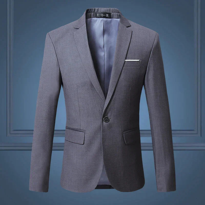 Blazer homme gris élégant, coupe ajustée, avec poche poitrine et deux poches à rabat, fond bleu. Veste formelle pour occasions spéciales.