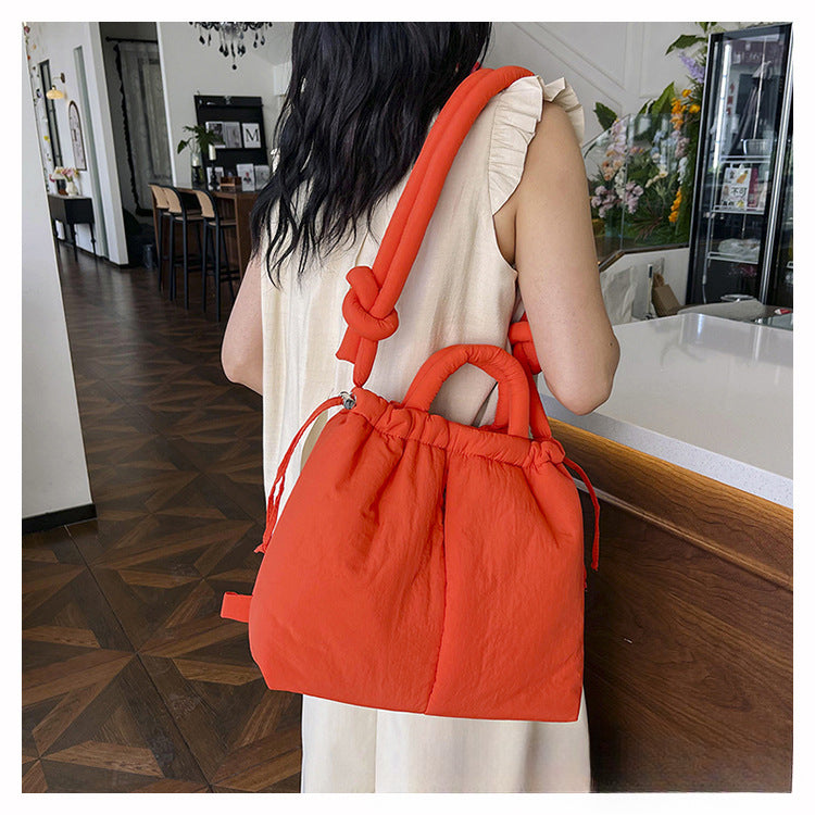 Femme portant un sac à main rouge vif en tissu matelassé, avec des poignées nouées, dans un intérieur moderne. Mode, accessoires, tendance.