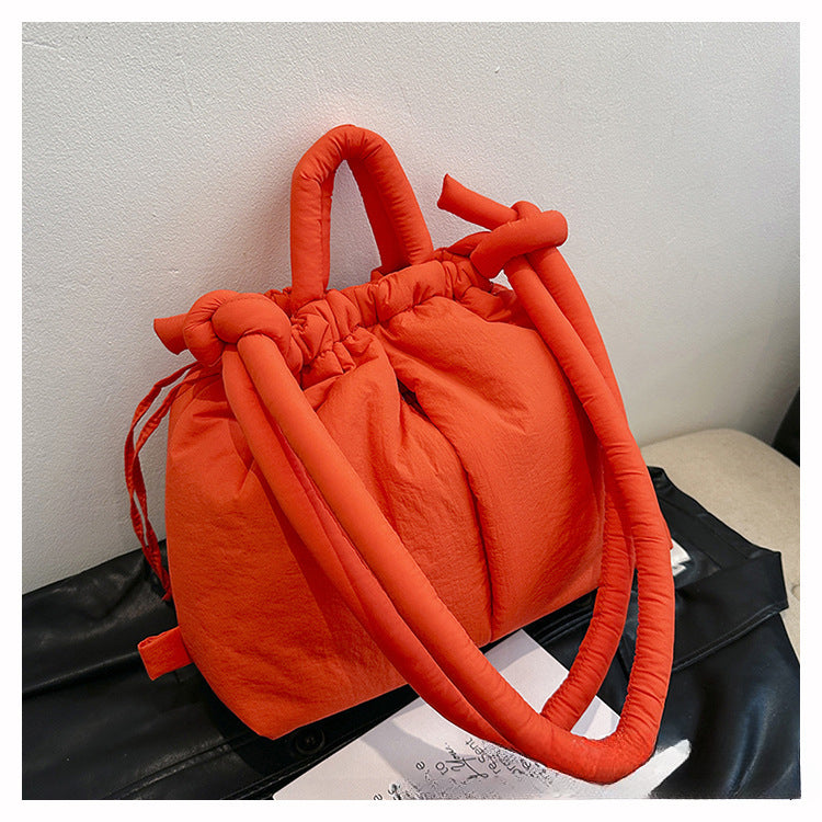 Sac à main orange vif avec poignées rembourrées, design moderne et élégant, posé sur une surface noire. Accessoire tendance pour femme.
