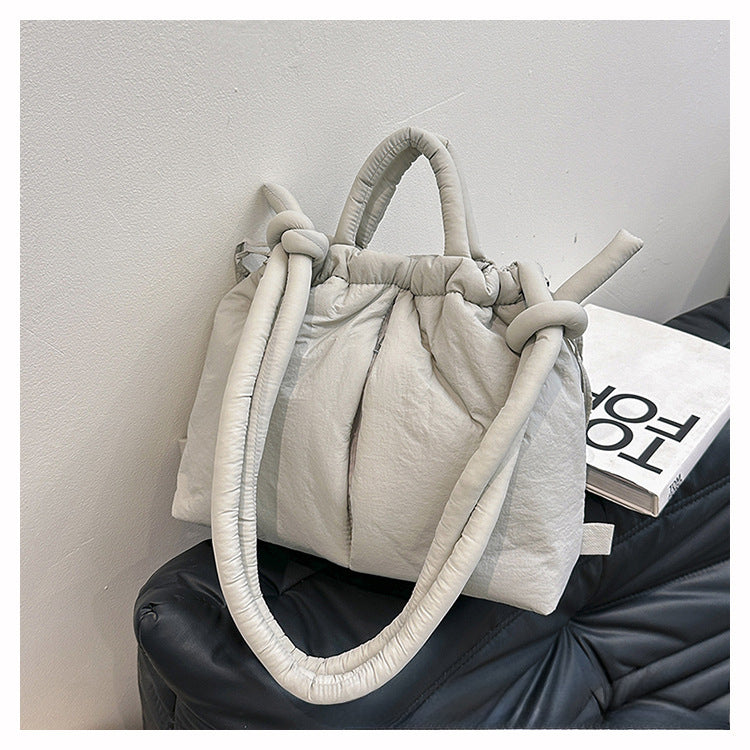 Sac à main matelassé gris clair avec poignées nouées, posé sur un canapé noir. Accessoire de mode élégant et tendance pour femmes.