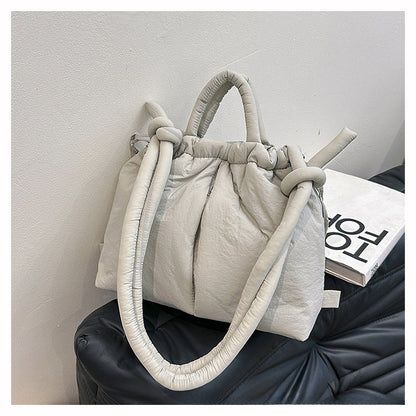 Sac à main matelassé gris clair avec poignées nouées, posé sur un canapé noir. Accessoire de mode élégant et tendance pour femmes.