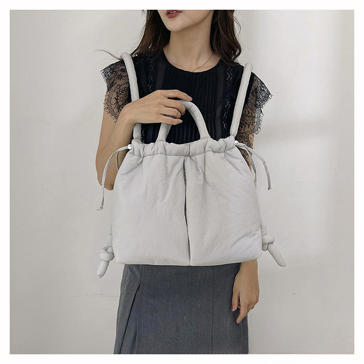 Femme tenant un grand sac à main blanc en tissu, style moderne et élégant, robe noire et jupe grise. Accessoire mode tendance pour femmes.