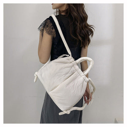 Femme portant un sac à main blanc matelassé, design moderne, bandoulière, robe noire élégante. Accessoire mode tendance, style chic et décontracté.