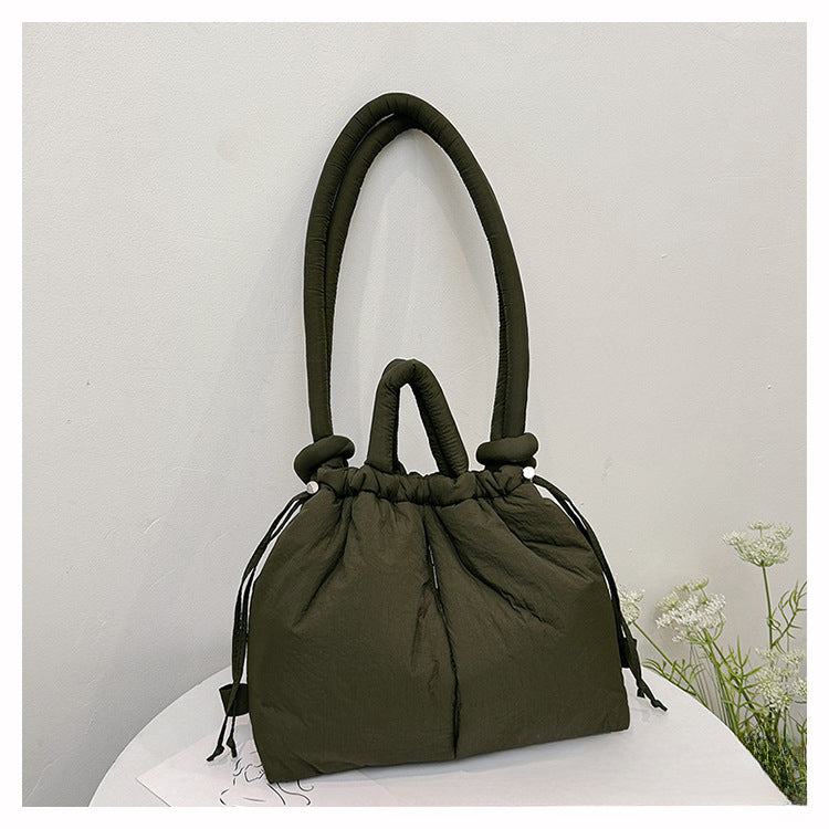 Sac à main vert olive élégant sur une table blanche, design moderne avec poignées rembourrées, idéal pour la mode féminine et les accessoires tendance.