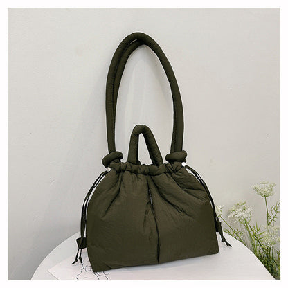 Sac à main vert olive élégant sur une table blanche, design moderne avec poignées rembourrées, idéal pour la mode féminine et les accessoires tendance.