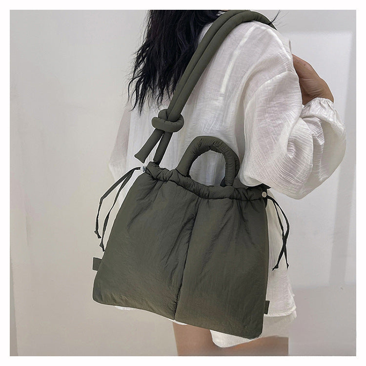 Sac à main matelassé vert olive porté par une femme en chemise blanche. Mode tendance, accessoire élégant, design moderne.