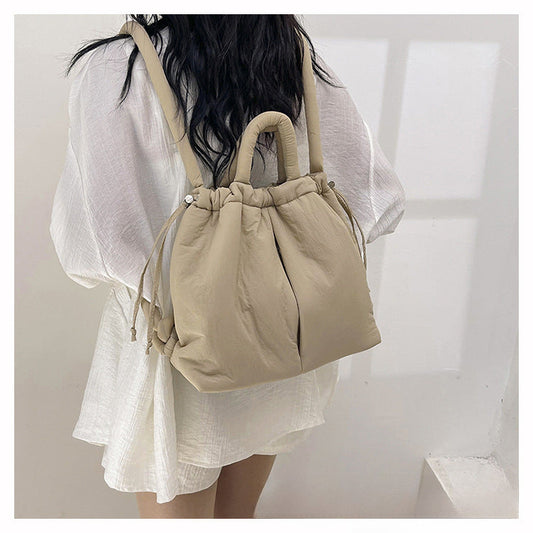 Sac à dos beige en tissu matelassé porté par une femme en robe blanche. Mode féminine, accessoire tendance, style décontracté et élégant.