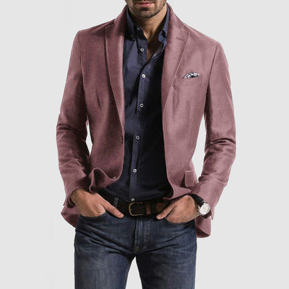 Homme portant une veste rose élégante, chemise bleue à motifs, jean décontracté, montre-bracelet et pochette, mode masculine chic et moderne.