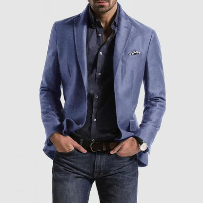 Homme portant une veste bleue élégante, chemise noire à motifs, jean décontracté, montre-bracelet et pochette, mode masculine moderne.