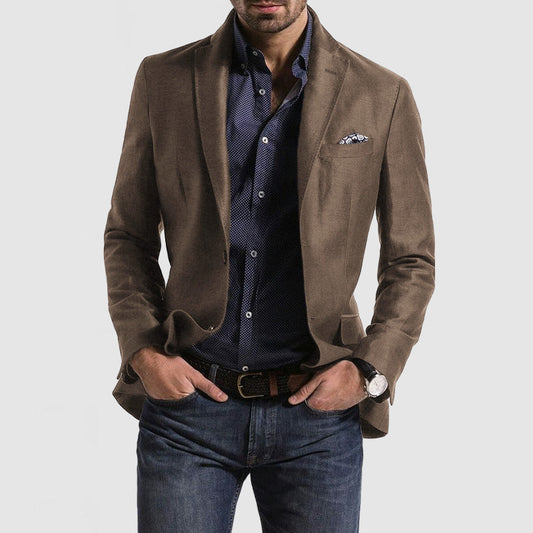 Homme en veste marron élégante, chemise bleue à motifs, jean décontracté, montre-bracelet, style mode masculine moderne, fond gris clair.