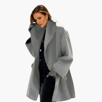 Femme portant un manteau gris élégant, coupe ample, sur fond blanc. Mode automne-hiver, tendance vestimentaire, style chic et moderne.