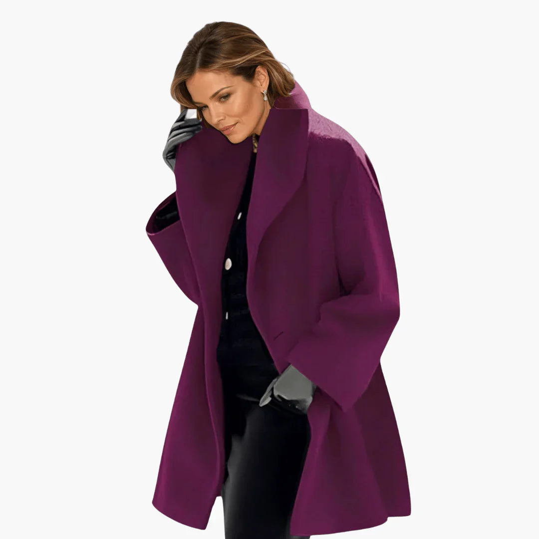 Femme portant un manteau violet élégant, gants gris et tenue noire, posant sur fond blanc. Mode automne-hiver, style chic et moderne.