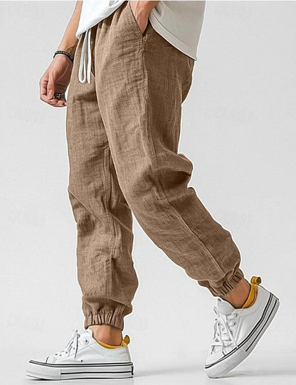 Brown jogger pants worn with white sneakers on a plain background