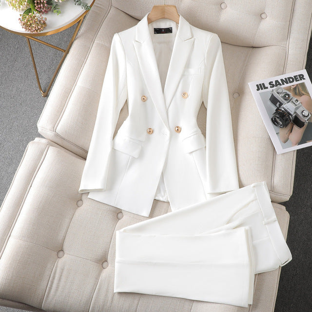 Costume blanc élégant pour femme, veste à double boutonnage et pantalon assorti, posé sur un canapé beige avec un magazine de mode.