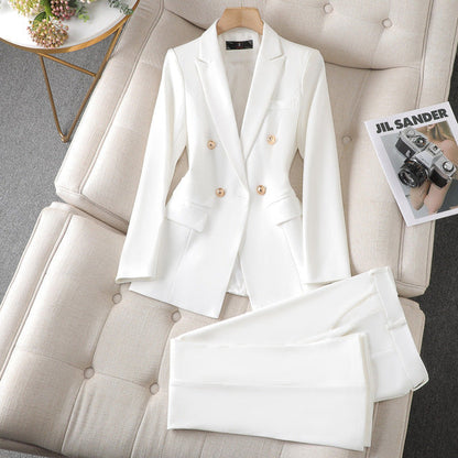 Costume blanc élégant pour femme, veste à double boutonnage et pantalon assorti, posé sur un canapé beige avec un magazine de mode.