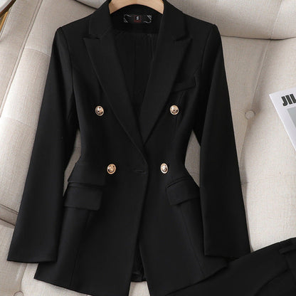 Veste blazer noire élégante à double boutonnage doré, posée sur un canapé beige, style chic et moderne pour femme, mode professionnelle.
