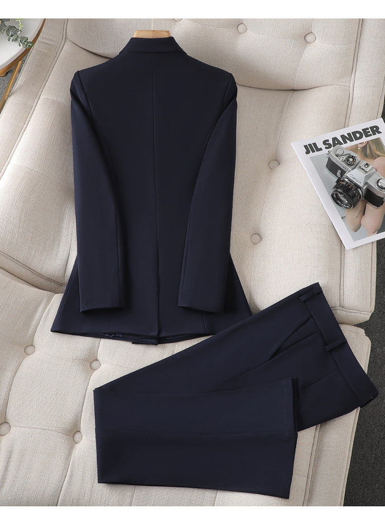 Costume bleu marine élégant pour homme, veste et pantalon, posé sur un canapé beige avec un magazine de mode à côté.