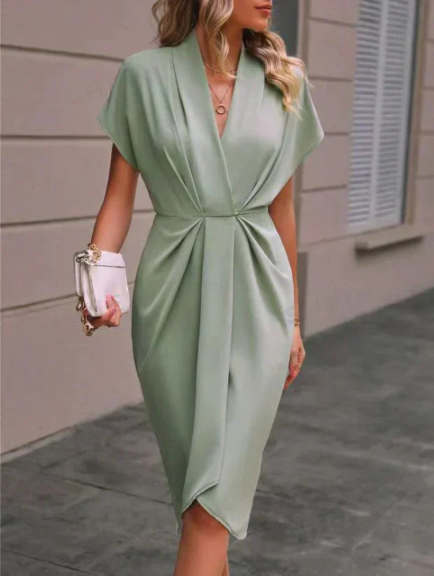 Robe verte élégante drapée, manches courtes, portée par une femme avec sac à main blanc. Mode féminine chic, tenue de soirée tendance.