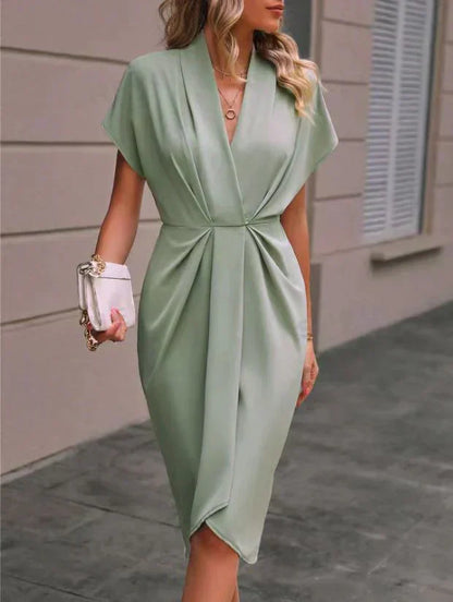 Robe verte élégante drapée, manches courtes, portée par une femme avec sac à main blanc. Mode féminine chic, tenue de soirée tendance.