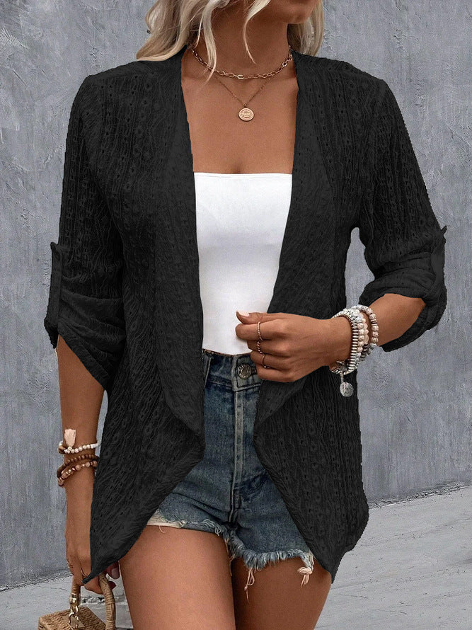 Femme en gilet noir texturé, top blanc, short en jean, accessoires en perles, fond gris. Mode décontractée, tenue estivale chic.