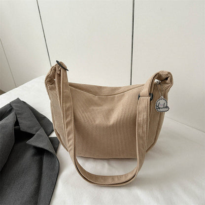 Sac à main beige en tissu côtelé avec breloque nuage, posé sur une surface blanche à côté d'une veste grise. Accessoire mode tendance.