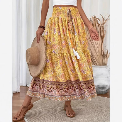 Jupe longue bohème jaune à motifs floraux, ceinture élastique, tenue estivale décontractée, femme tenant un chapeau de paille, sandales marron.