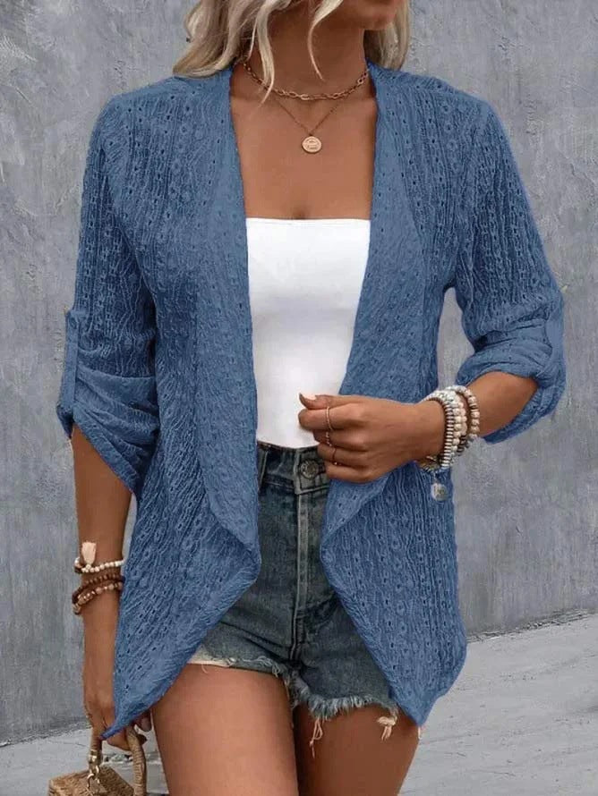 Femme portant un cardigan bleu en dentelle, débardeur blanc, short en jean, accessoires en perles. Mode décontractée, tendance été.