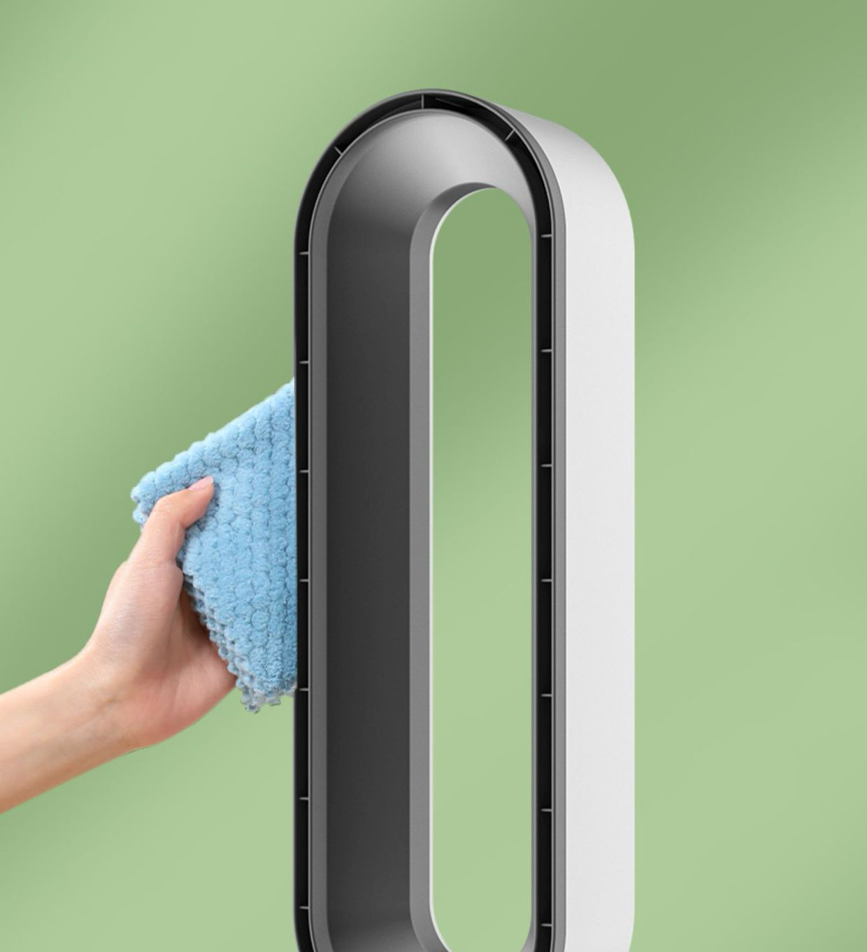 Main nettoyant un ventilateur sans pales moderne avec un chiffon bleu sur fond vert. Design élégant, technologie innovante, entretien facile.