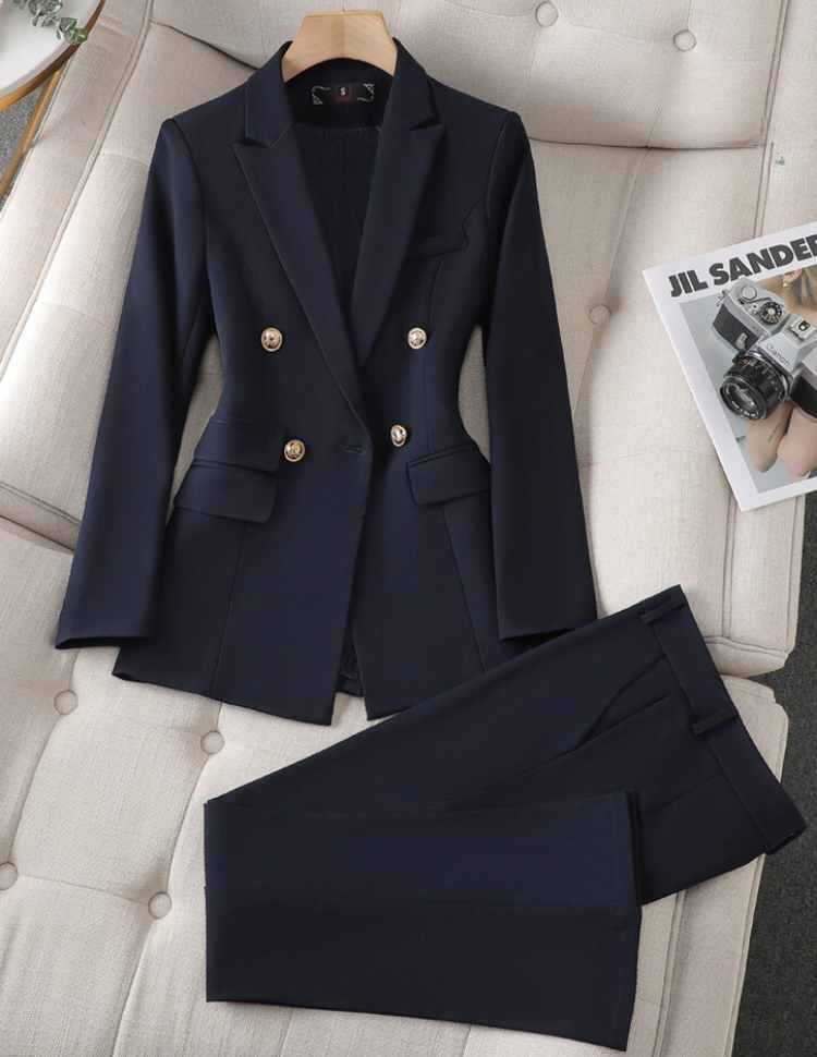 Costume femme bleu marine élégant avec boutons dorés, posé sur un canapé beige. Magazine de photographie à côté. Mode professionnelle chic.
