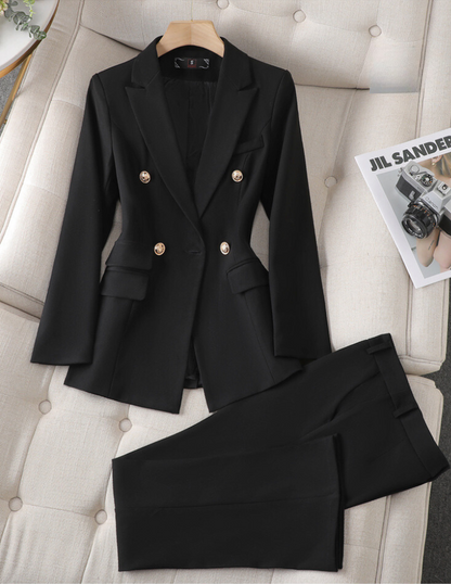 Costume noir élégant pour femme avec blazer à boutons dorés et pantalon assorti, posé sur un canapé beige, à côté d'un magazine de mode.
