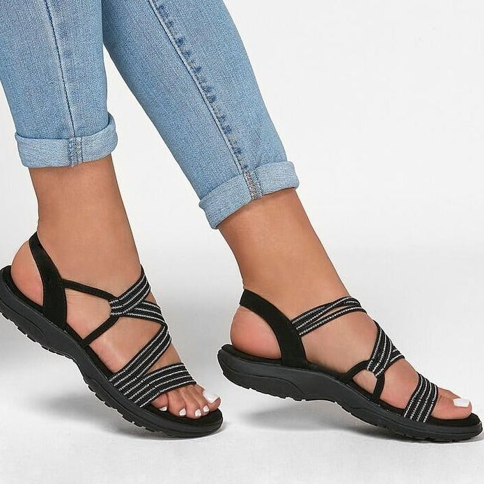Sandales noires à brides croisées pour femme, portées avec un jean bleu clair. Chaussures d'été confortables et élégantes.