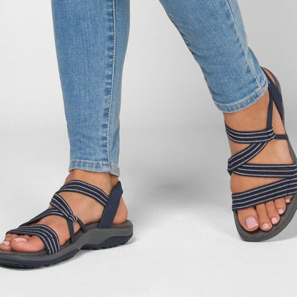 Jeans bleus et sandales de randonnée noires à lanières croisées, confortables et modernes, sur fond blanc. Mode estivale décontractée.