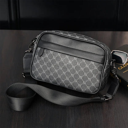 Sacoche en cuir noir et gris avec motif géométrique, bandoulière ajustable, posée sur une table en bois sombre. Accessoire mode homme élégant.