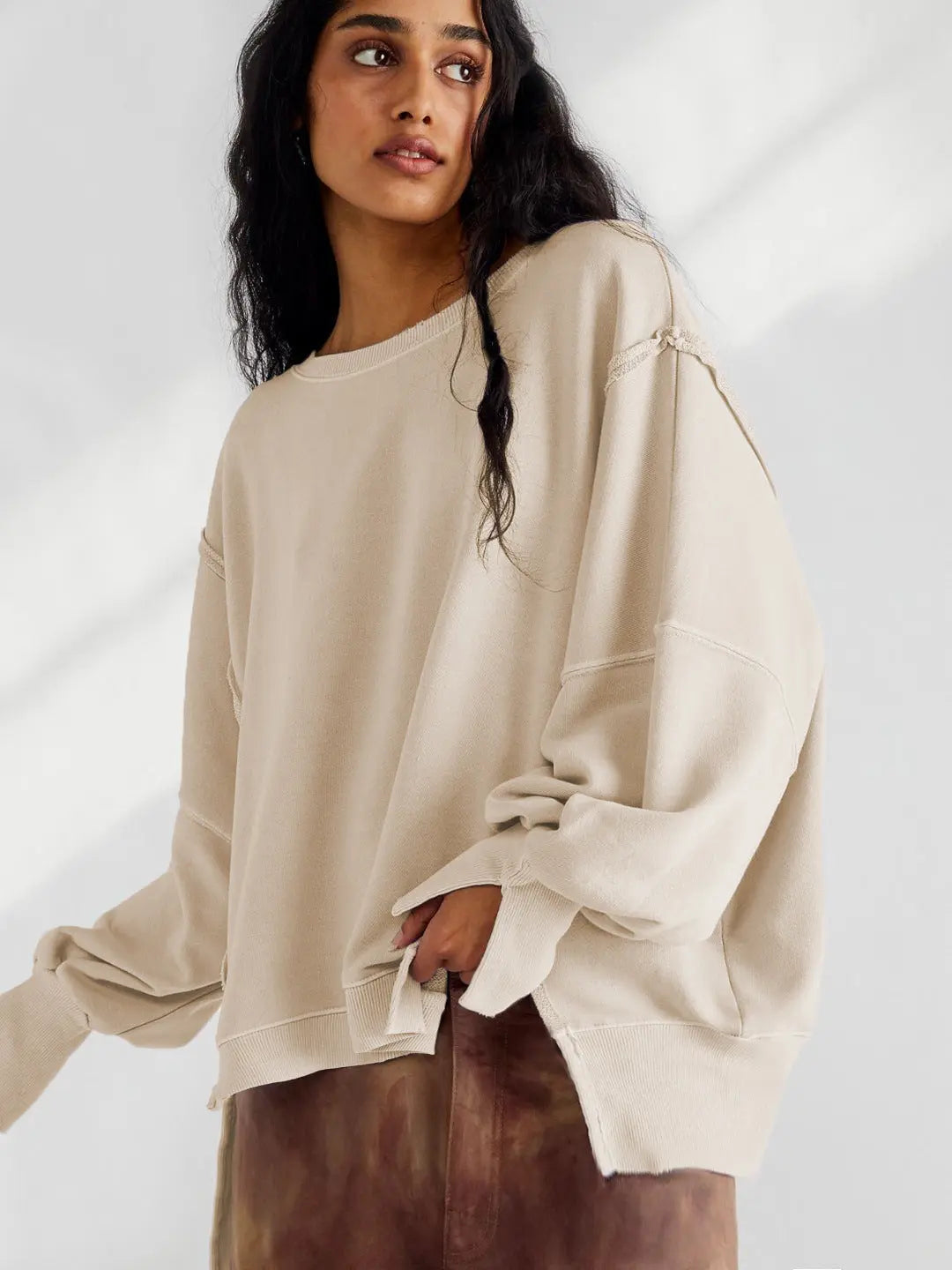 Jeune femme portant un pull beige oversize, manches longues, style décontracté, sur fond neutre. Mode automne-hiver, tendance confortable.