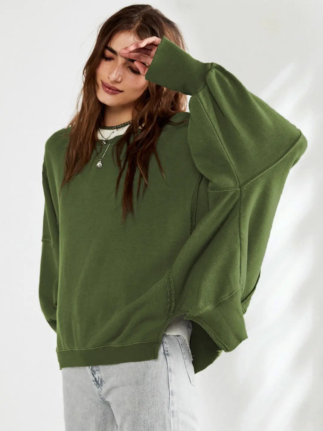 Femme portant un pull vert ample, manches larges, avec un jean clair. Mode décontractée, tendance automne, style confortable.