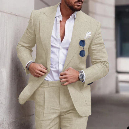 Homme en costume beige élégant, chemise blanche ouverte, lunettes de soleil accrochées, montre-bracelet argentée, style urbain chic.