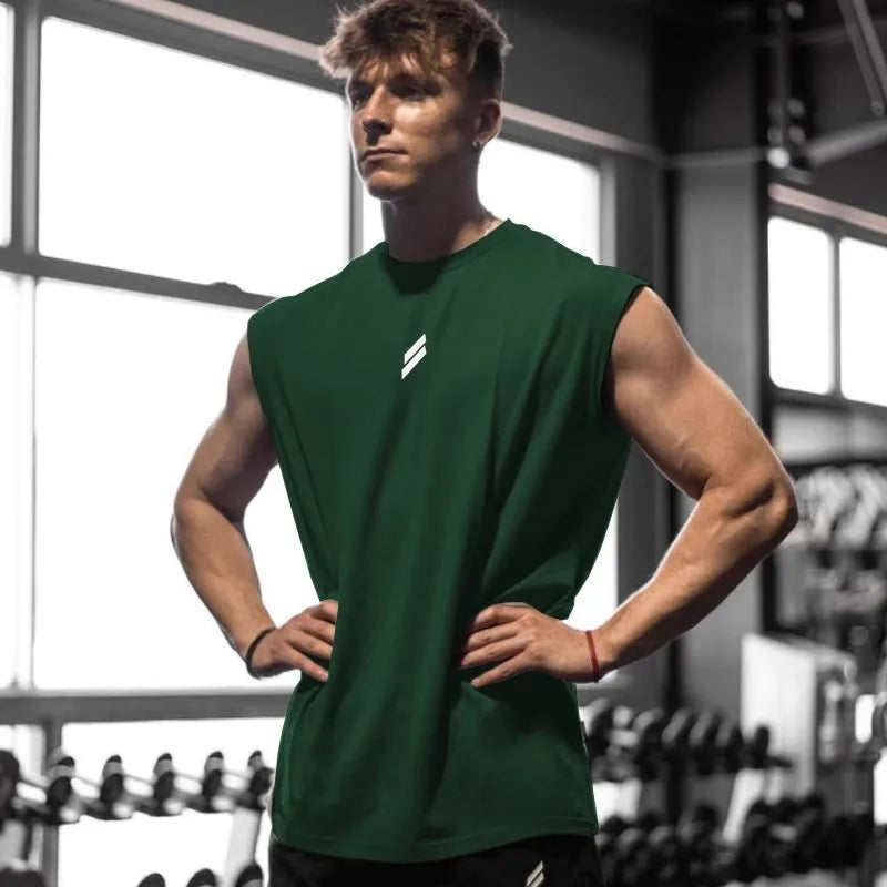Ung mand i grøn trænings-T-shirt står i fitnesscenter, omgivet af vægte. Fitness, styrketræning, sund livsstil, muskuløs fysik.
