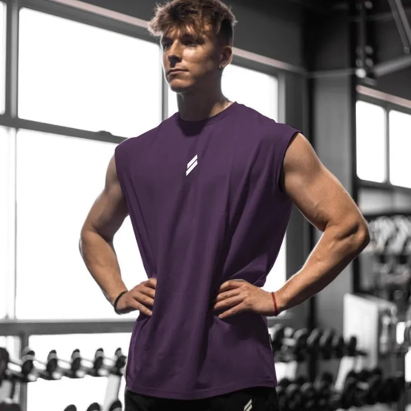 Mand i lilla træningsshirt i fitnesscenter, står med hænderne på hofterne foran vægtstativ. Styrketræning, fitnessmode, muskuløs fysik.