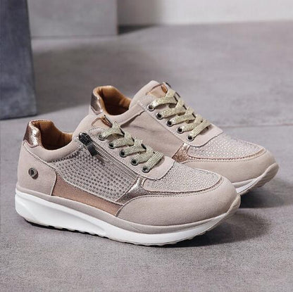 Chaussures de sport beiges pour femmes avec lacets dorés et fermeture éclair latérale, semelle blanche antidérapante, design moderne et élégant.
