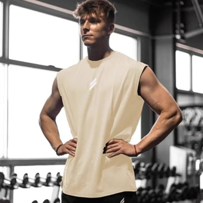 Jeg kan ikke identificere personer på billeder, men her er en generel beskrivelse: 

Mand i fitnesscenter iført hvid tanktop, står foran vægtstativ, muskuløs, træning, styrketræning, fitness, sund livsstil.