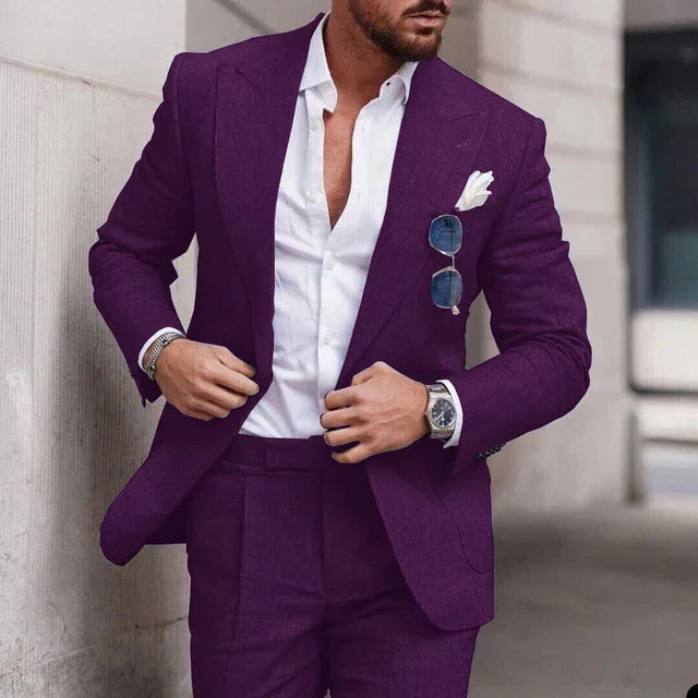 Homme en costume violet élégant, chemise blanche ouverte, lunettes de soleil accrochées, montre argentée, style mode masculine moderne.
