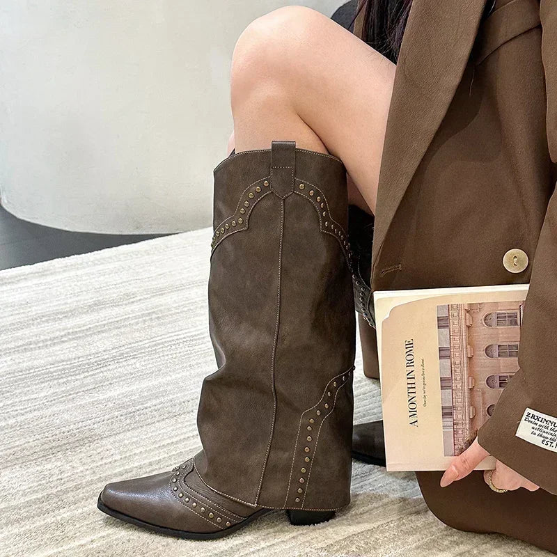 Brune cowboystøvler med nitter, bæres af en person i brun jakke, sidder på gulvtæppe og holder en bog. Trendy fodtøj, mode, efterårsstil.