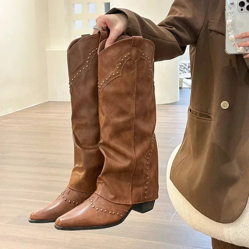 Brune cowboystøvler med nitter, holdt af person i brun jakke. Stilfulde læderstøvler, perfekt til mode og western-look.