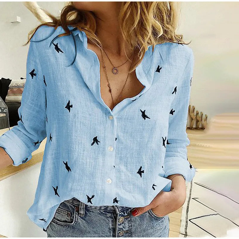 Femme portant une chemise en lin bleu clair avec motifs d'oiseaux noirs, manches retroussées, col ouvert, associée à un jean décontracté.