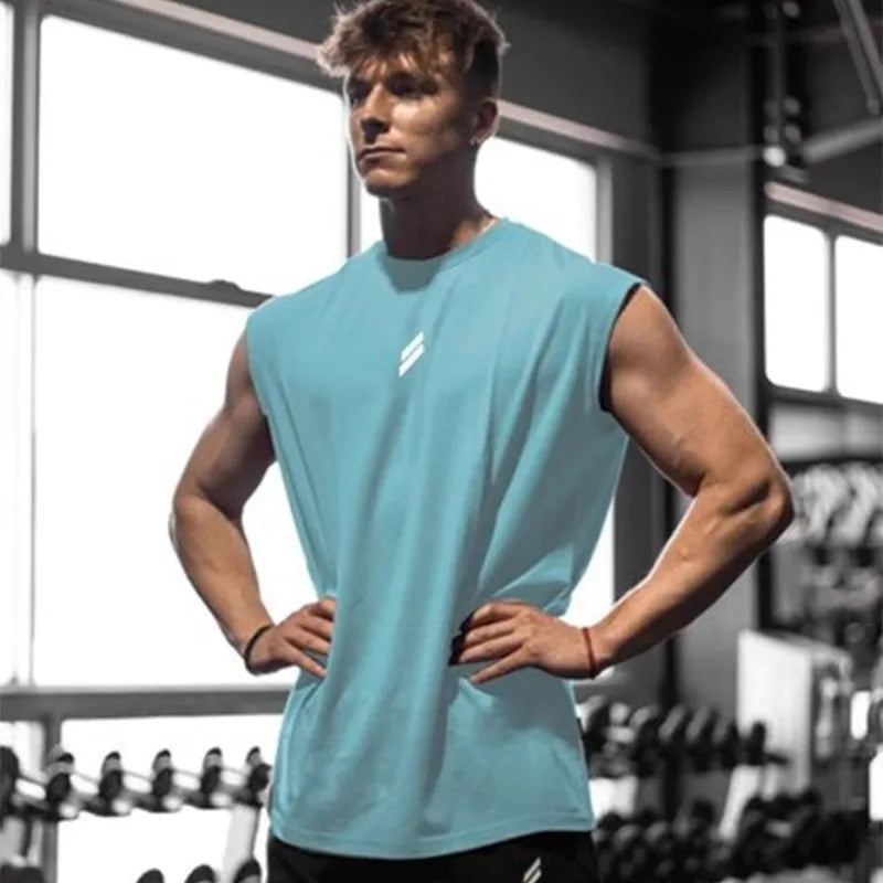 Mand i lyseblå tanktop træner i fitnesscenter, omgivet af vægte. Fitness, styrketræning, muskelopbygning, sund livsstil.