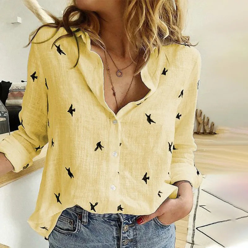 Femme portant une chemise jaune à motifs d'oiseaux noirs, manches retroussées, associée à un jean décontracté. Mode tendance, style décontracté.